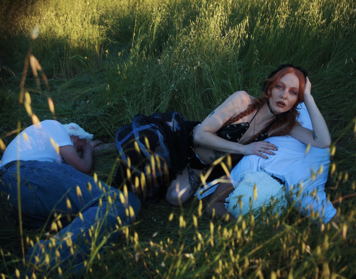 Mistress Luna reclining in black shepherdess styling among submissive sheep figures