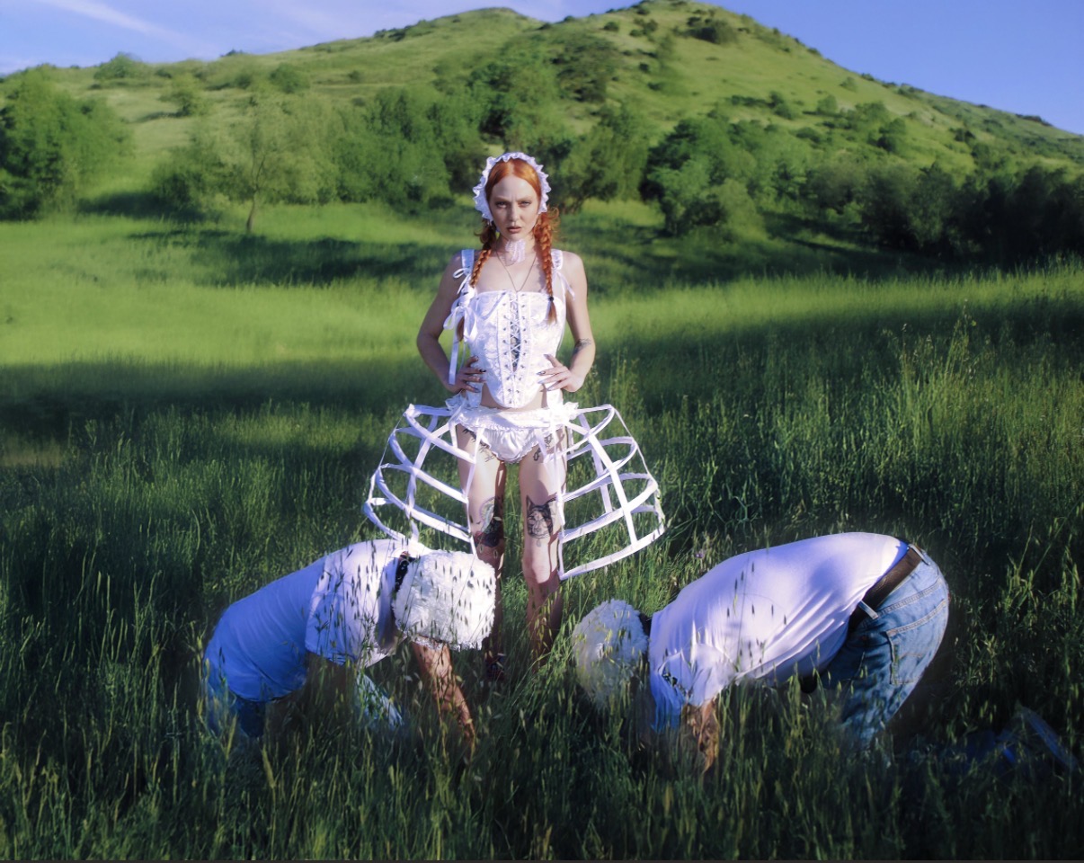 Mistress Luna standing centered in white shepherdess styling with two bowed submissive sheep figures